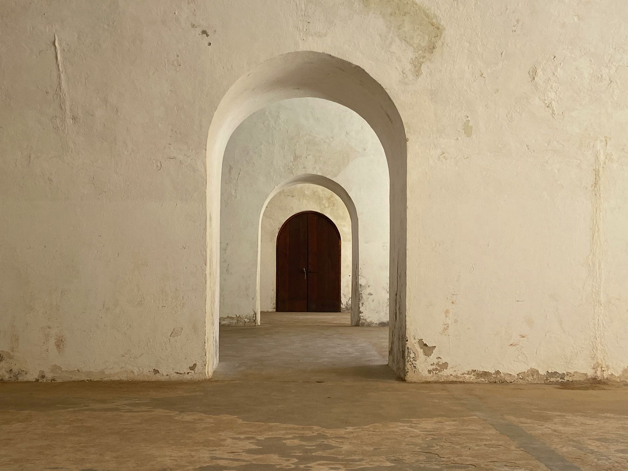 A series of pale stone arches leading to a wooden doorway