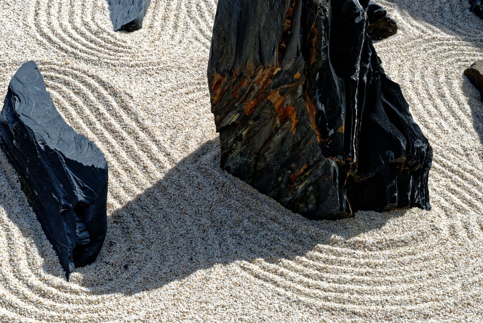 Curving lines raked through pale sand around dark garden stones